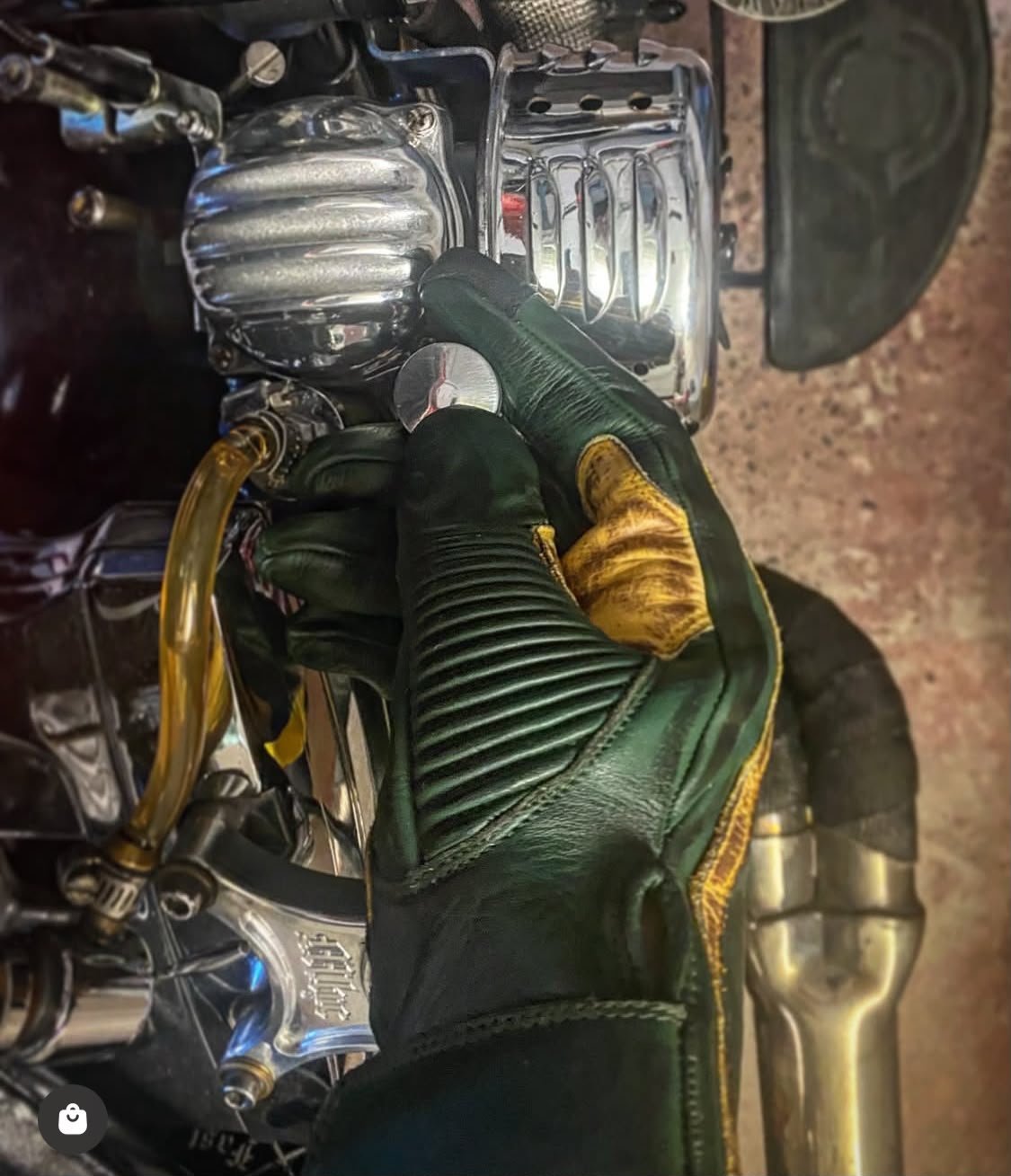 1971 Le Mans Motorcycle Gloves — Green Patina Vintage Racing Hold Fast 1971 Le Mans green patinated motorcycle glove worn on a handlebar, showing the contrasting palm and gathered wrist.